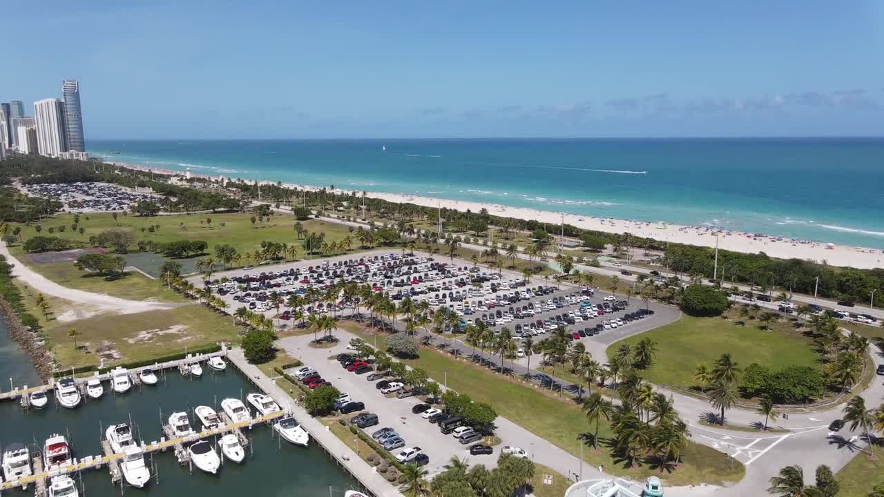 Aerial drone shot of boats moored at the harbor, cars in the parking area, and a beautiful seascape under a clear blue sky in Hawaii.