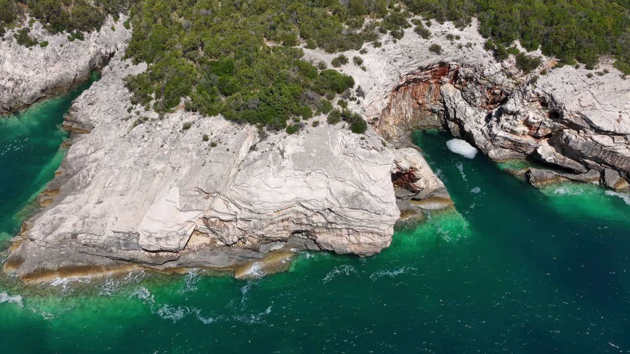 Vista aerea ravvicinata di scogliere rocciose stratificate, acqua turchese vibrante e una grotta marina a Dugi Otok, Croazia