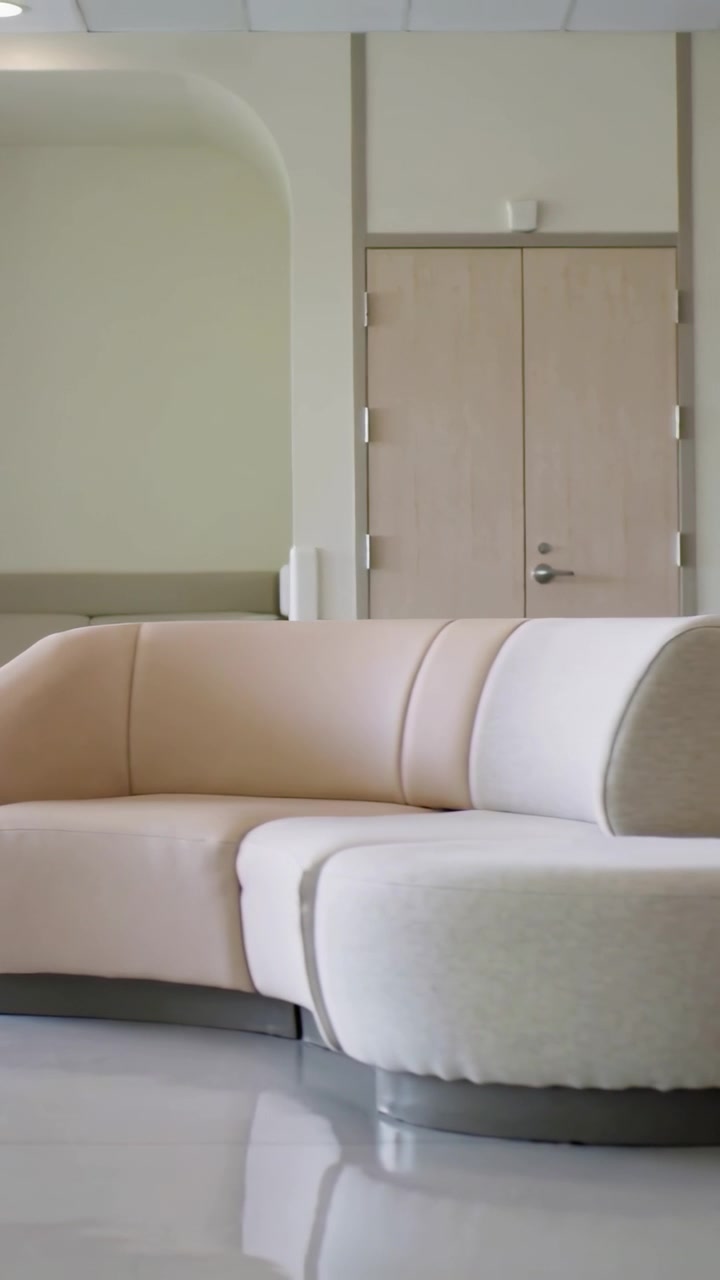Vertical video: Panning camera revealing curved beige sectional and bench in lounge to show design