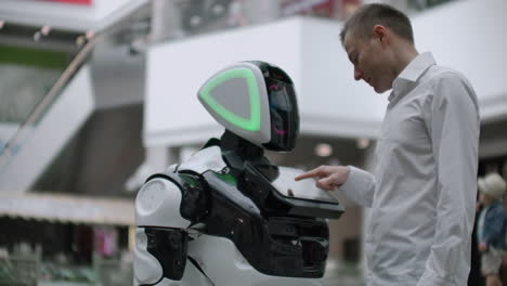 el hombre en el centro comercial se comunica con un asesor robot. tienda moderna y vendedor robot. robot ayuda a un hombre en el centro comercial.