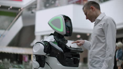 the man in the shopping mall communicate with a robot advisor. modern shop and robot seller. robot helps a man in the mall.