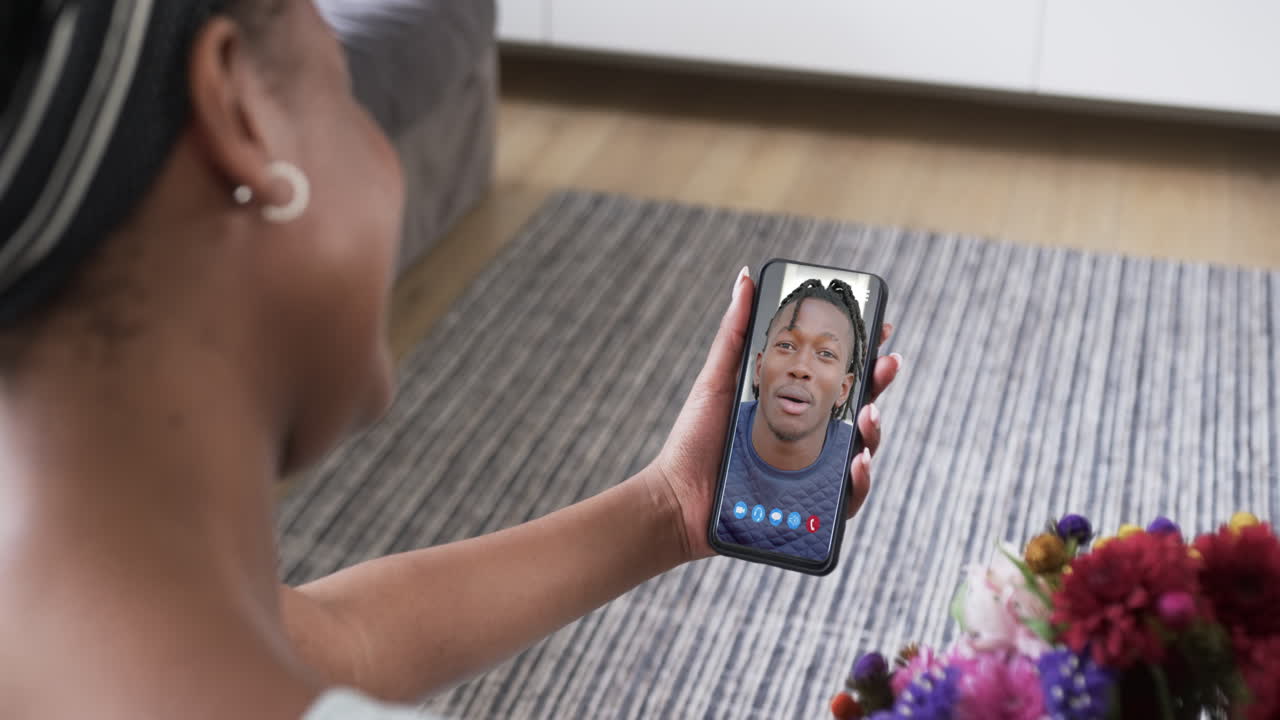 mujer biracial sosteniendo un teléfono inteligente con un hombre biracial hablando en la pantalla