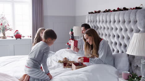 padres abriendo regalos de los niños mientras se sientan en la cama intercambiando regalos el día de navidad