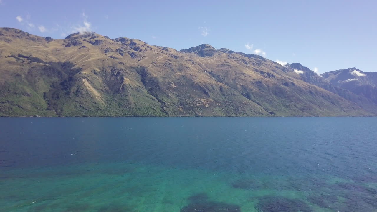 Aerial drone footage flying out of silhouetted forest to reveal a vast blue and green lake surrounded by mountains