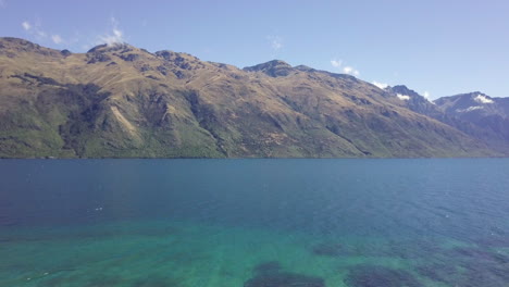 aerial drone footage flying out of silhouetted forest to reveal a vast blue and green lake surrounded by mountains