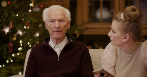 hombre mayor hablando mientras su nieta usa el teléfono durante la navidad 3