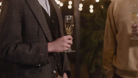 close up of two unrecognizable men holding champagne glasses and talking to each other anew year's eve party