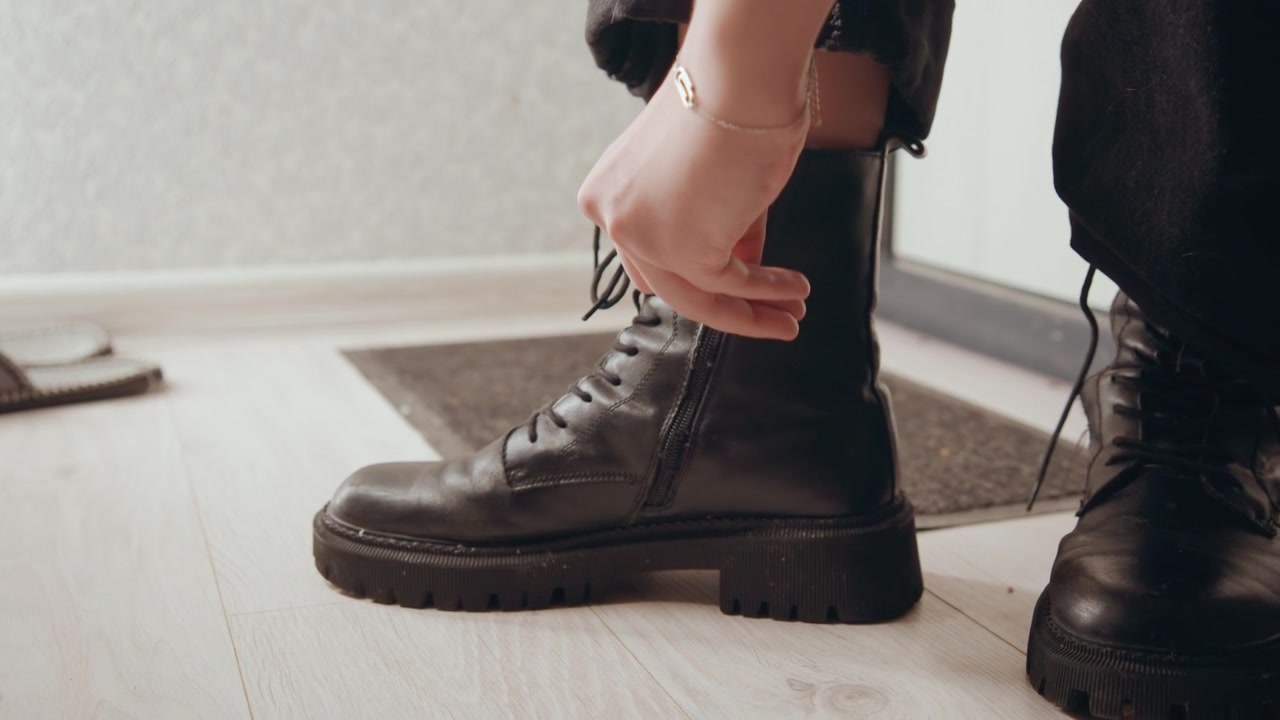 Boots preparation scene. Leather footwear tied on floor. Casual moment of adjusting leather boots before departure. Preparing to leave as leather shoes are carefully secured near door area