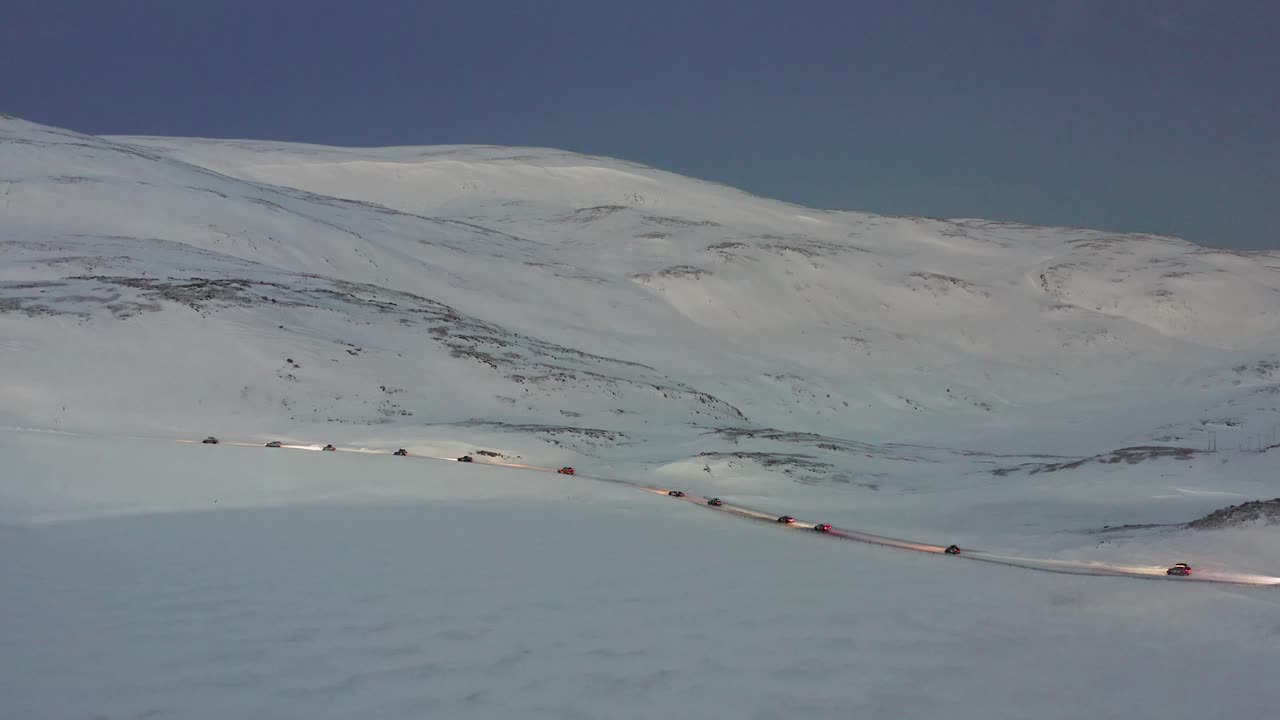 A convoy of cars driving on an icy road towards the Nordkapp, Norway during the midwinter solstice. High angle orbit shot