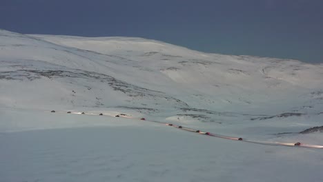 a convoy of cars driving on an icy road towards the nordkapp, norway during the midwinter solstice. high angle orbit shot