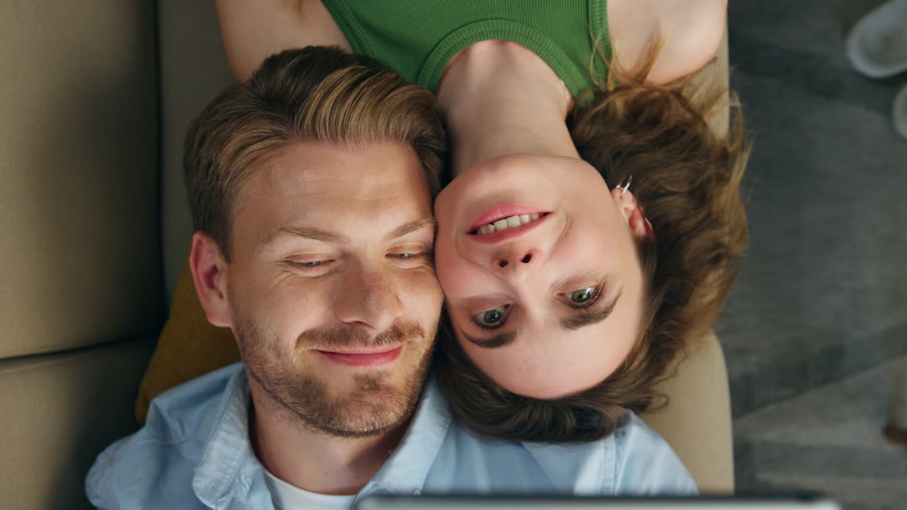 Coppia innamorata che si fa un selfie sdraiata sul divano, vista dall'alto. Coppia che prova un'app per maschere facciali
