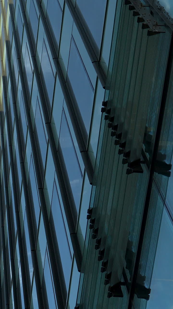 Inquadratura verticale dal basso di un moderno edificio per uffici con pannelli di vetro e strutture in acciaio che riflettono il cielo blu. Perfetto per contenuti di architettura aziendale e urbana.
