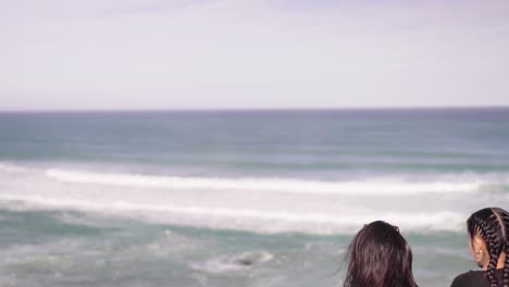 Two-females-looking-out-towards-ocean-tides-arriving-on-shore-along-Great-Ocean-Road,-Victoria,-Australia