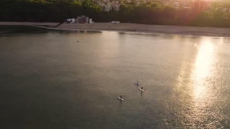 drone shot of family stand up paddle boarding in tranquil bay during golden sunset light - backwards flight