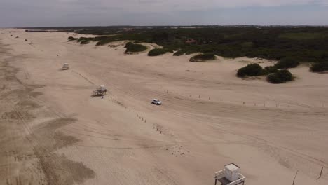 antena: vehículos de 4 ruedas conduciendo y saliendo de la playa de arena durante el día soleado - mar de las pampas, argentina
