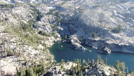 sunny 4k stabilized drone aerial shot shows an alpine lake at the base of a mountain range in the california wilderness with remaining snow during sunset in summer as a camping and hiking destination