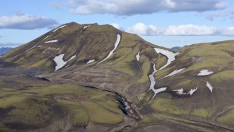 aerial drone view with a backward left movement, facing a green mountain in landmannalaugar near bláhylur lake