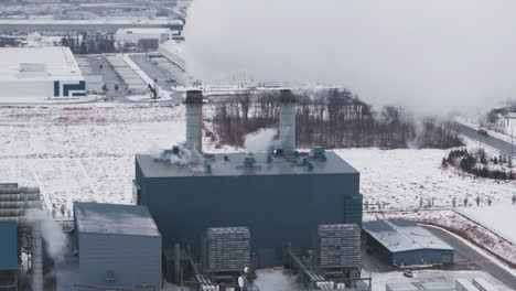 an industrial plant with multiple smokestacks, surrounded by snow-covered ground, aerial view