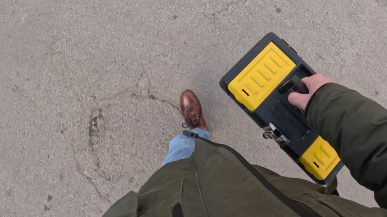 A walking perspective looking down at a person carrying tools in hand, capturing movement and purpose in motion.