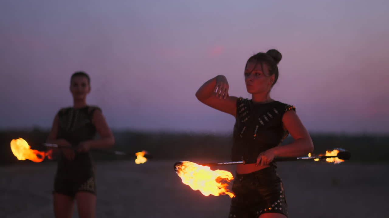 Women with fire at sunset on the sand dance and show tricks against the beautiful sky in slow motion