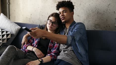 cute happy couple of young hipsters cuddling on the couch, trying to find a perfect tv channel. leisure time, enjoying youth, living together. relationship goals.