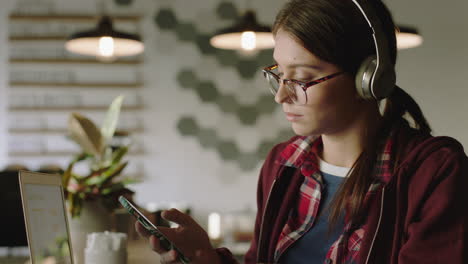 young woman student using smartphone in cafe drinking coffee working late on research project browsing online messages networking enjoying mobile phone communication listening to music