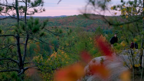 Hiker-walks-away-from-edge-of-cliff-while-looking-out-over-scenic-fall-landscape,-Algonquin-Park,-Ontario-Canada