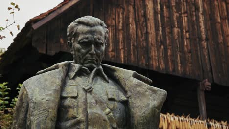 bronze statue of josip broz tito in front of a rustic building in kumrovec, croatia
