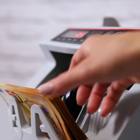 female teller putting money into currency counting machine at cash department, close up
