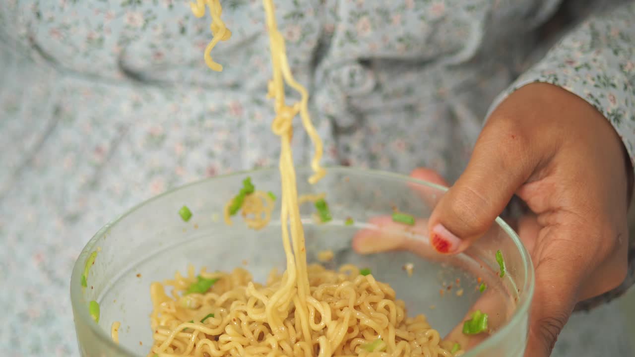 Close-up of a person stirring instant noodles in a glass bowl