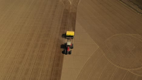 seguimiento de la vista aérea de un tractor rojo de dos ruedas sembrando semillas en línea recta en un campo agrícola con una sembradora amarilla durante la primavera