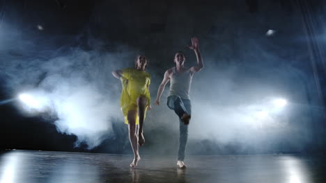 a man and a woman dance together a funny dance in jeans and a yellow dress on stage in smoke. musical.