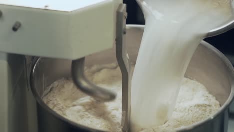 the baker pours the sourdough into a machine that mixes the bread dough