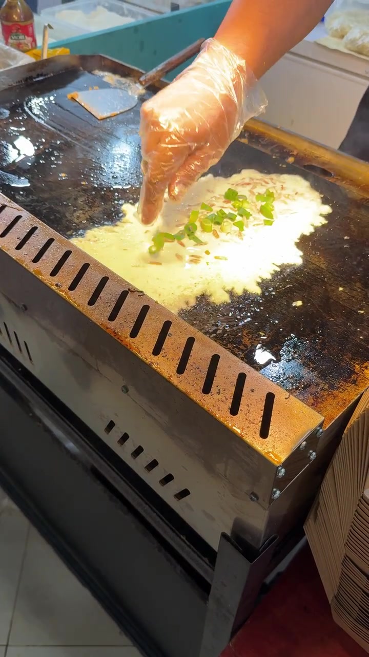 Chef Sprinkling Chopped Green Onions onto Cooking Omelet on Griddle