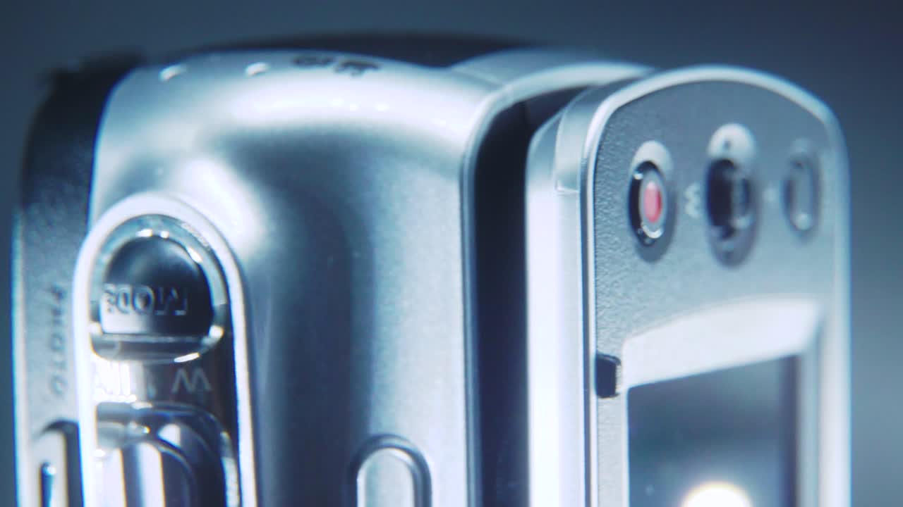 una toma macro de una cámara de video, una videocámara plateada en un soporte giratorio de 360, iluminación de estudio, video de 4k en cámara lenta, pantalla abierta, grabación, zoom y botones de menú