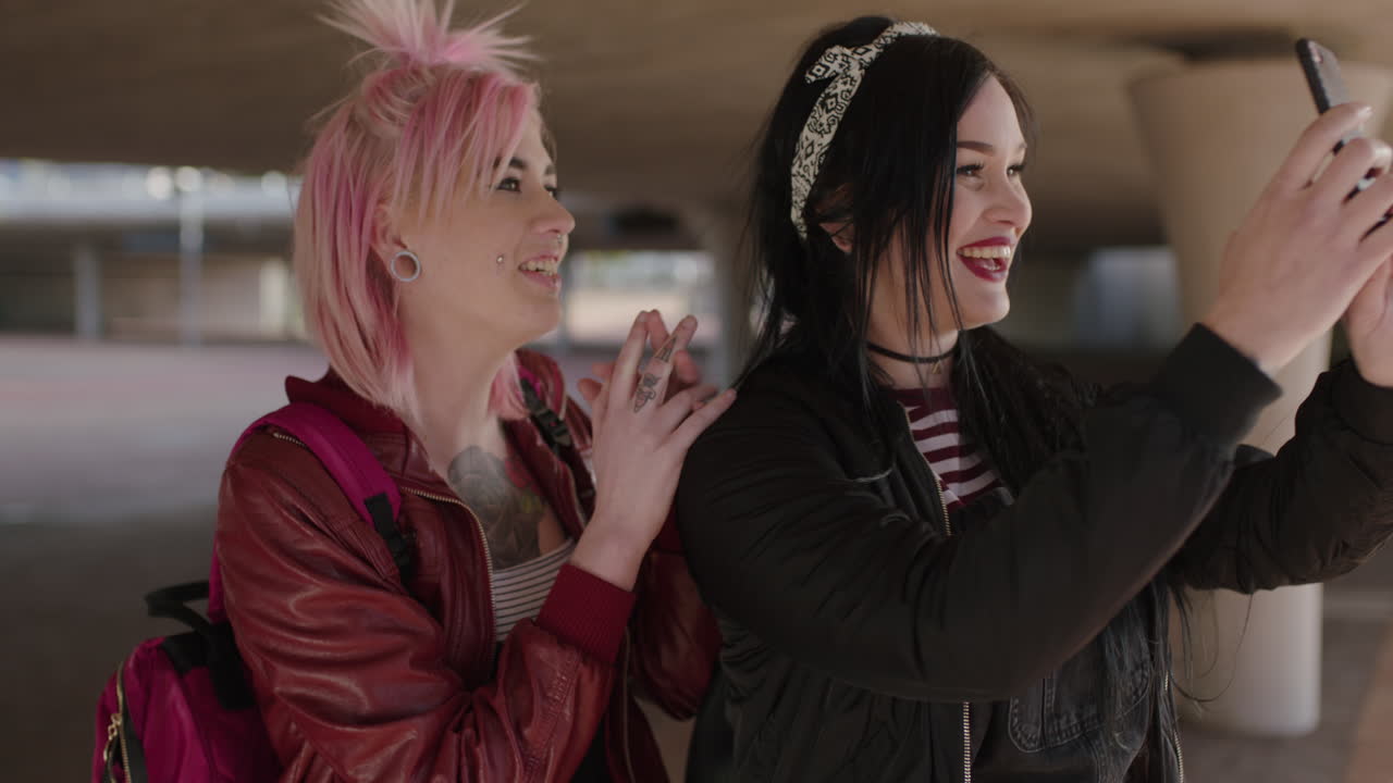 retrato alegre de dos amigas auténticas vestidas con moda grunge alternativa sonriendo usando el teléfono posando para una foto selfie