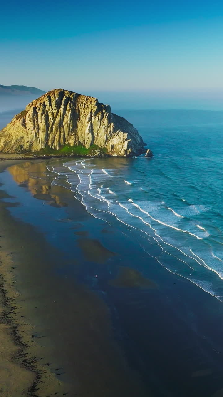 Beautiful white foamy waves coming to the sandy shore with a rock in the middle. Blue waters of Pacific ocean on bright sunny day. Vertical video