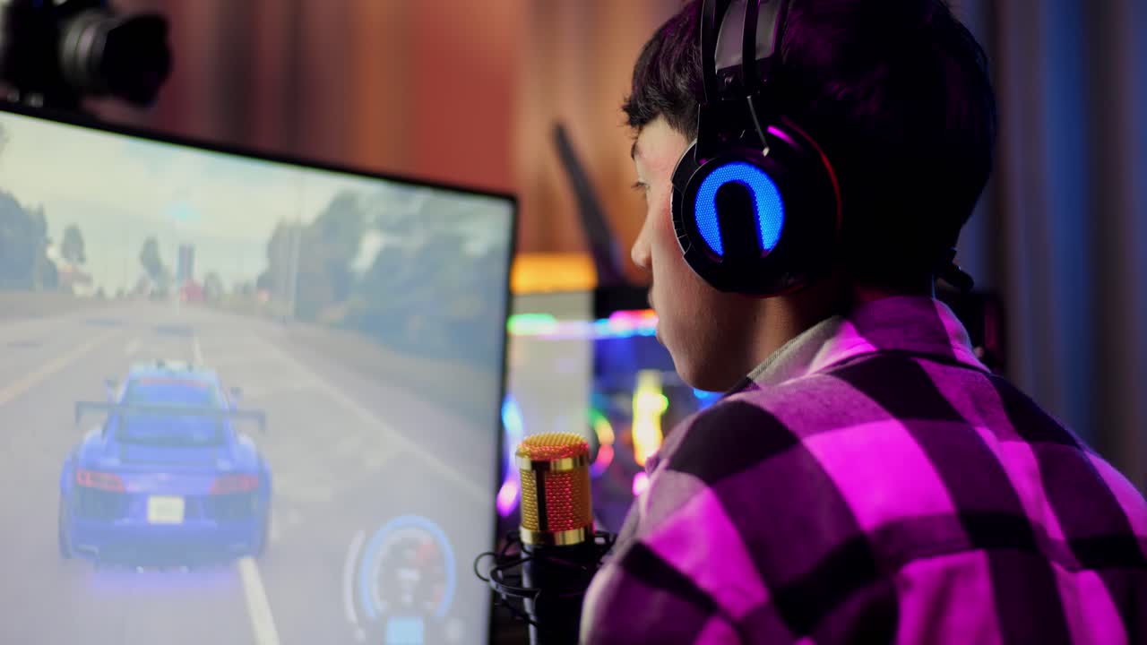 개인용 컴퓨터에서 네트워크를 통해 자동차 레이싱 게임을하는 동안 스트레칭하는 아시아 소년 스트리머의 근접 후면 뷰 라이브 스트리밍 비디오 게임, rgb led 스트립 라이트에 의해 조명 된 책상