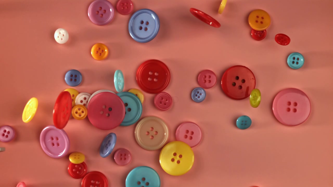 Bottoni colorati che cadono e si spargono su uno sfondo rosa.