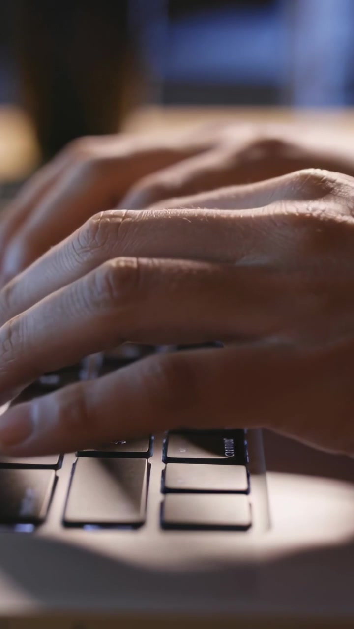 Vertical video: Typing hands moving from hover to pressing keys on desk keyboard writing email