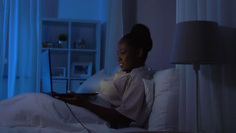 African-Woman-with-Laptop-in-Bed-at-Home-at-Night.technology,-internet,-communication-and-people-concept-young-african-american-woman-with-laptop-computer-lying-in-bed-at-home-at-night