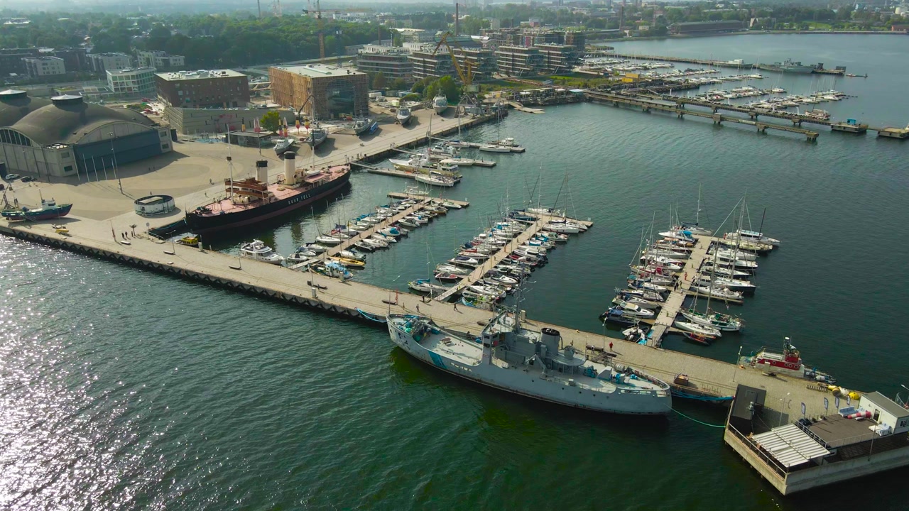 Aerial drone footage ascending and flying higher in front of a modern and beautiful sailboat and yacht harbor where boats are docked on the pier during a summer sunny day. Apartment buildings visible.