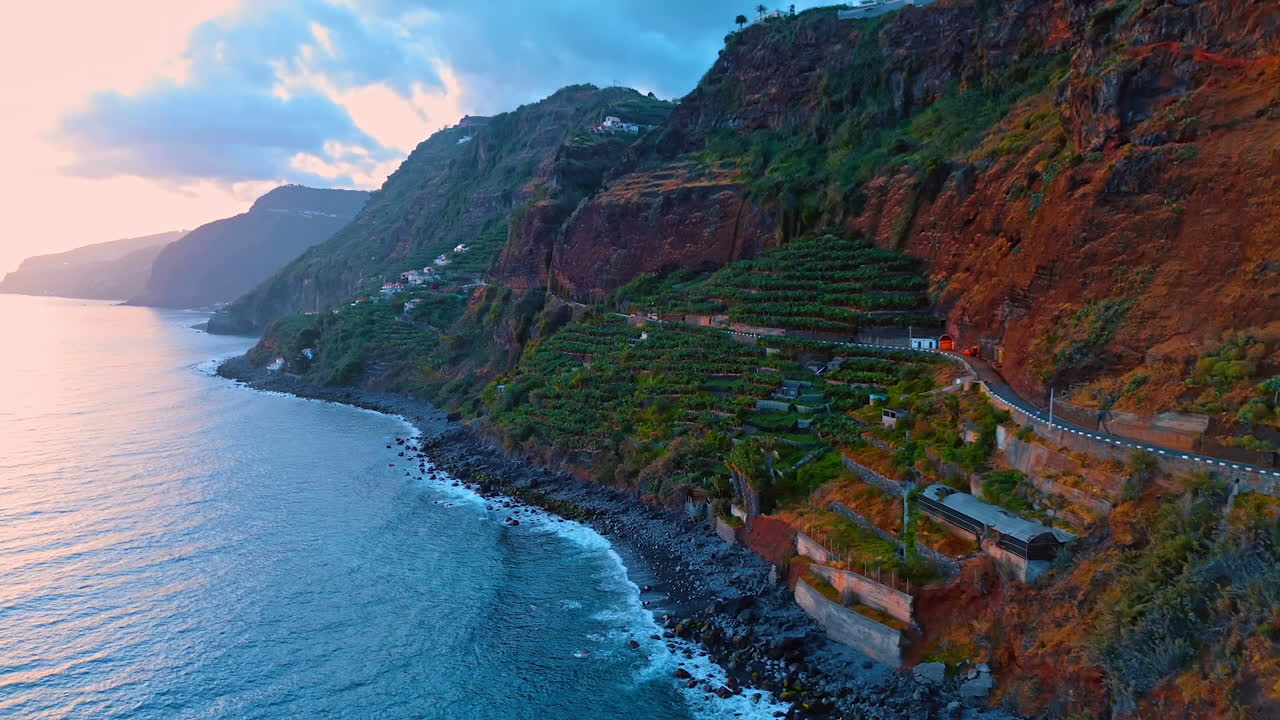 Amazing high mountains with gardens on the slopes. The Atlantic Ocean hits the rocks at the coast of the Madeira Islands, Portugal. Drone footage.