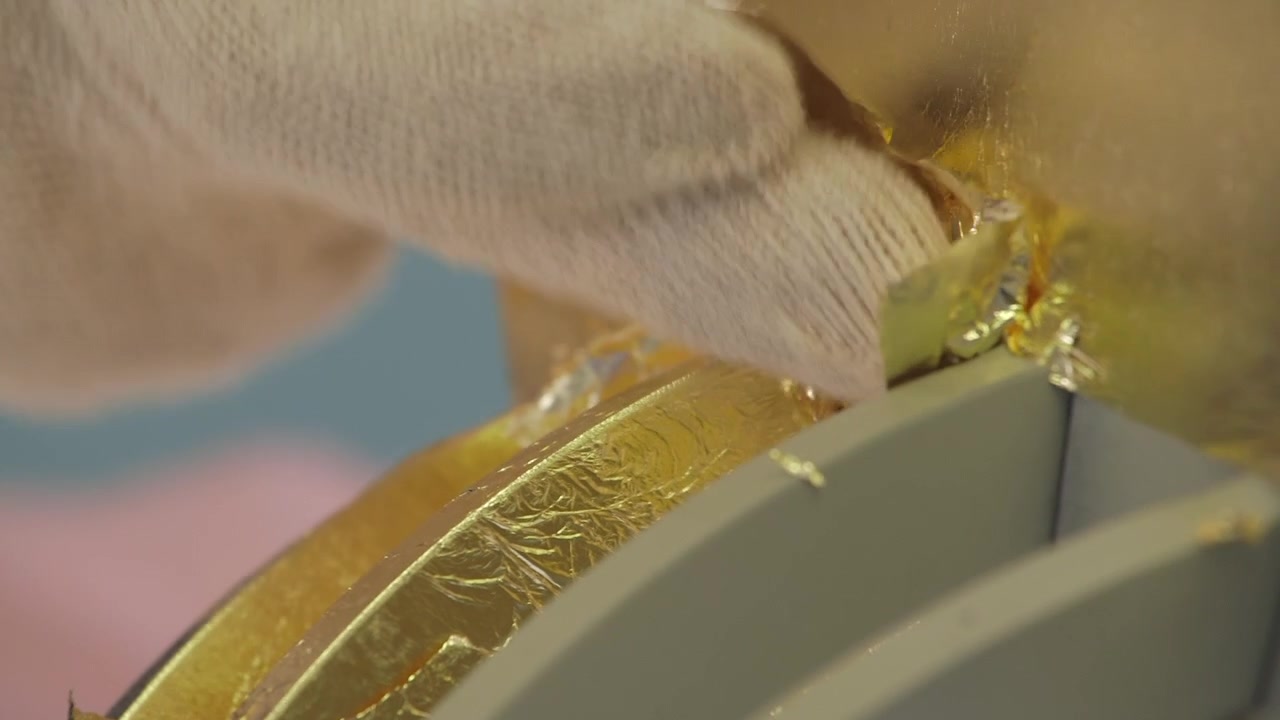 Close-up of a skilled artisan using a special brush to apply delicate gold leaf onto a decorative surface during a traditional gilding process.