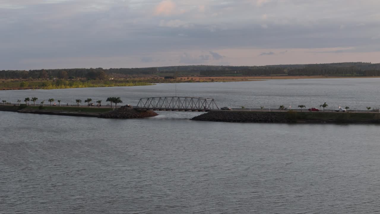 A serene river with a bridge under an overcast sky at dusk reflects the harmony between nature and urban development in Federacion, Entre Ríos, Argentina