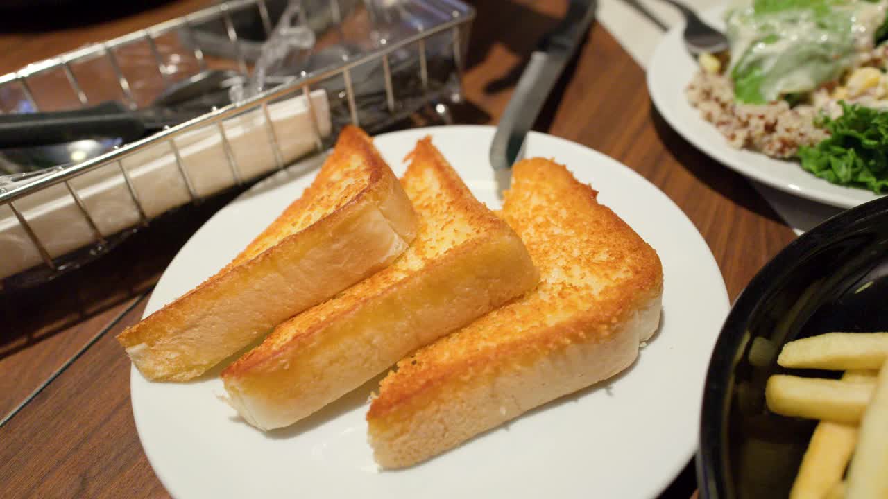 Close-up of hand grabbing toasted garlic bread at casual restaurant table, warm indoor lighting