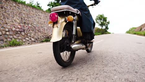 woman riding vintage motorbike through street with low traffic, close up low angle view