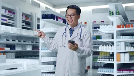 asian male doctor with stethoscope using smartphone and pointing to the side while standing in pharmacy