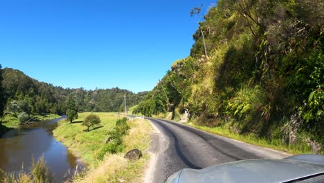 driving on the road with scenery of green rocky mountain in taranaki, new zealand on a sunny day