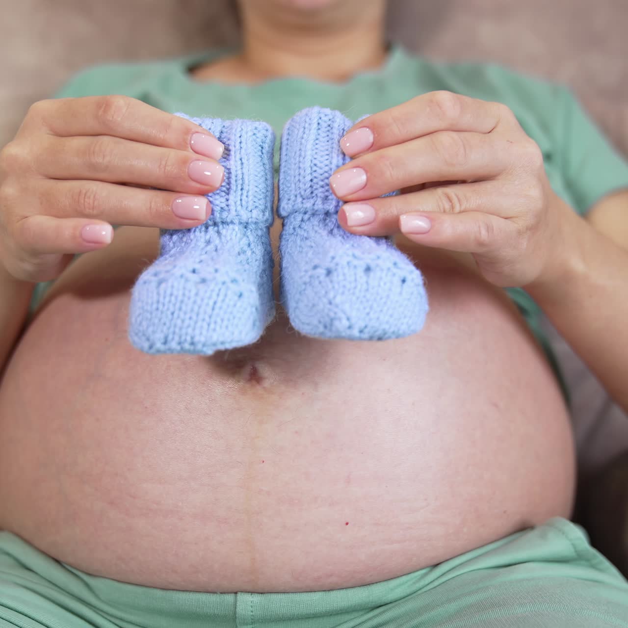 Il ventre scoperto di una futura mamma. Donna incinta che gioca amorevolmente con dei calzini lavorati a maglia sulla pancia. Primo piano